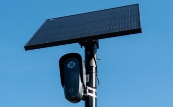 Close-up view of a license plate camera and solar panel mounted on a pole, with the sky in the background.