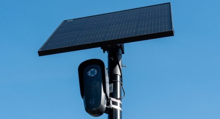 Close-up view of a license plate camera and solar panel mounted on a pole, with the sky in the background.
