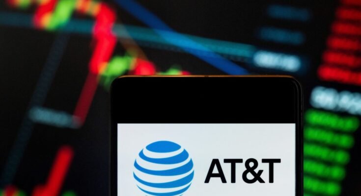 AT&T logo displayed on a smartphone with a stock exchange index graph in the background.