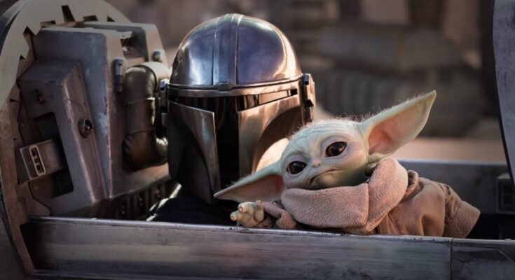 mandolorian in full armor and helmet with little green yoda-like figure sitting in a spacecraft