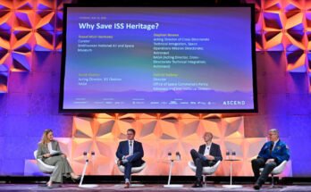 Four people sit on a colorfully-lit stage under a large screen displaying their panel title, names and titles.