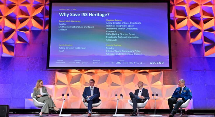 Four people sit on a colorfully-lit stage under a large screen displaying their panel title, names and titles.