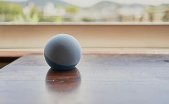An Amazon Echo Dot smart speaker on a table by a window.