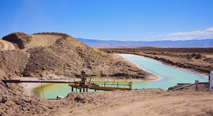 Image of a dry, plant less desert area. In amidst large lumps of soil sit a human-shaped pond of vivid blue water.