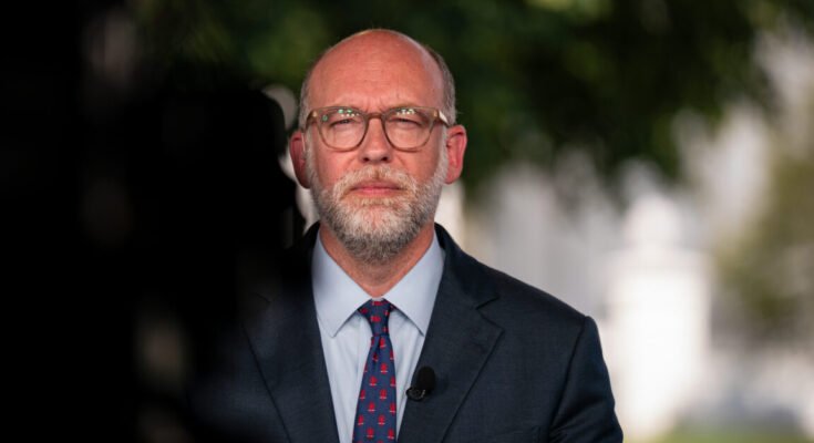 Image of a white man in a suit with glasses.