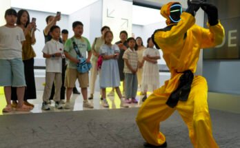 Children watch a martial arts performance by Unitree robots at a humanoid robot store on June 1, 2026 in Zhengzhou, Henan Province of China. The robot is wearing yellow martial arts clothing.