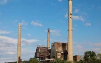 A river with a large power plant with three smokestacks on the shore.