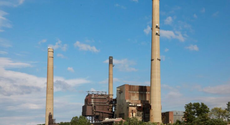 A river with a large power plant with three smokestacks on the shore.