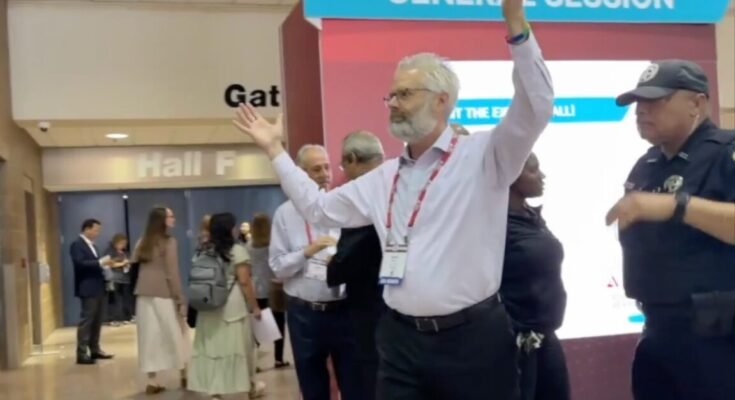 Police escort Dr. Steven Kuhn out of a medical conference in New Orleans for handling out copies
