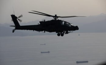 A US Army AH-64 Apache helicopter gunship can be seen flying over commercial ships in the Strait of Hormuz during a patrol on April 17, 2026.