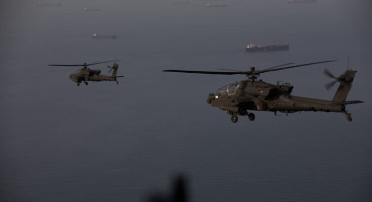 AH-64 Apache helicopters fly above the Strait of Hormuz during a patrol, April 17. Commercial ships are visible on the water below.