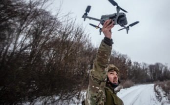 A Ukrainian soldier holds reconnaissance drone above his head on the Sumy front in January 2026. The background shows a wintry landscape with bare trees.