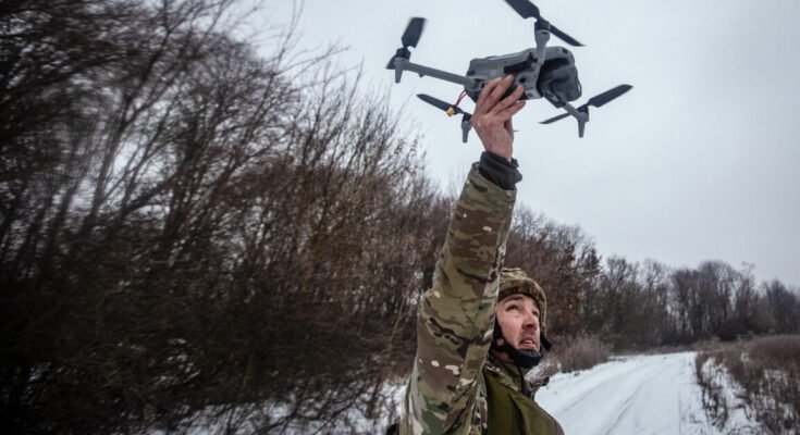 A Ukrainian soldier holds reconnaissance drone above his head on the Sumy front in January 2026. The background shows a wintry landscape with bare trees.