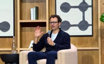 Dario Amodei sits on a chair on stage and gestures as he talks.