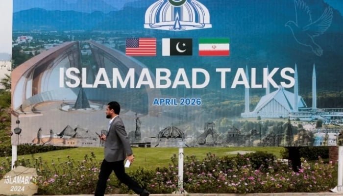 ایک شخص میڈیا سنٹر کے قریب ایک بل بورڈ کے پاس سے گزر رہا ہے جب 11 اپریل 2026 کو امریکہ اور ایران کے وفود کی اسلام آباد میں امن بات چیت متوقع ہے۔ - رائٹرز
